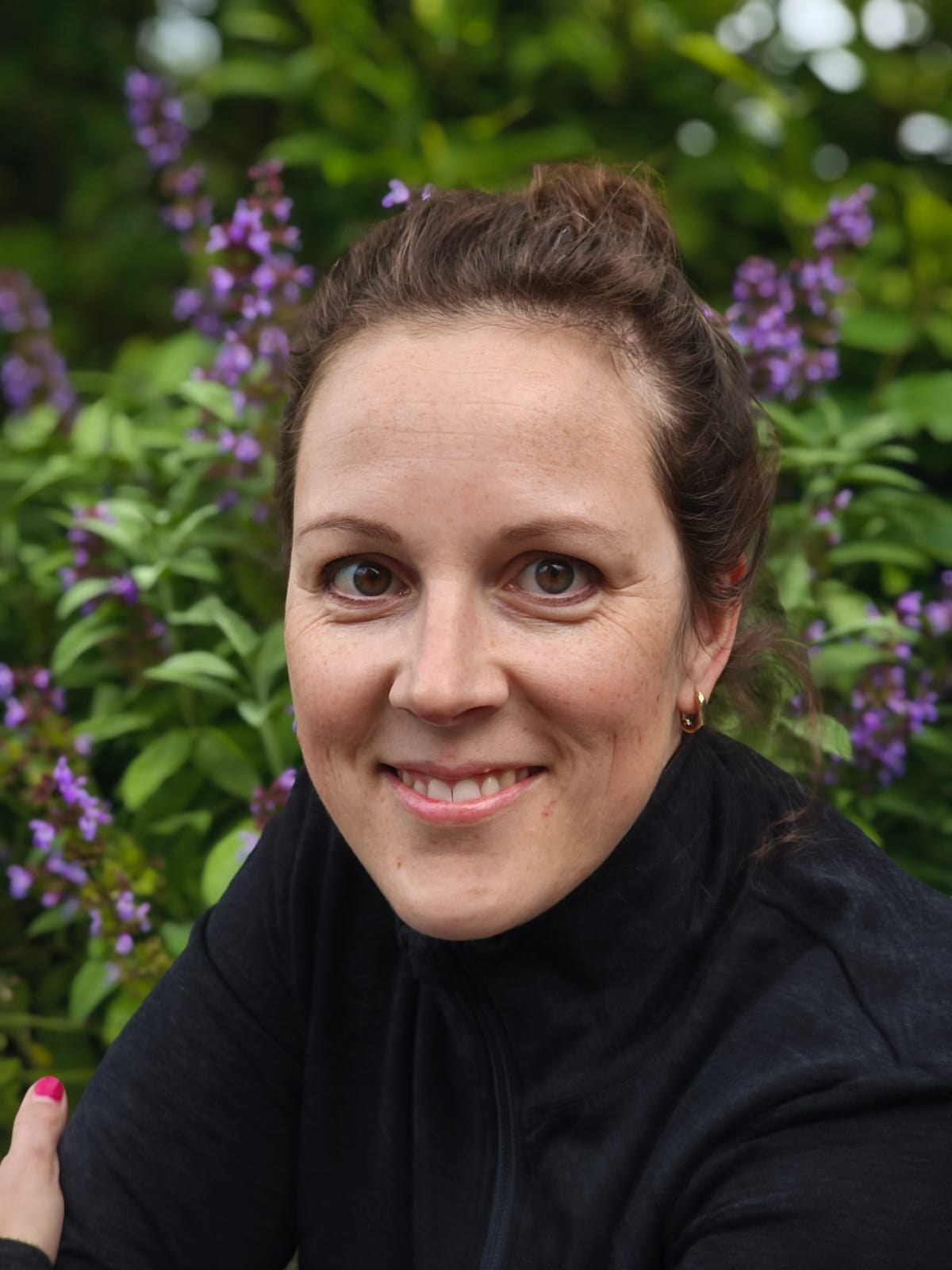 Porträt von Nicole Santiago Maria vor grünen Pflanzen und violetten Blüten